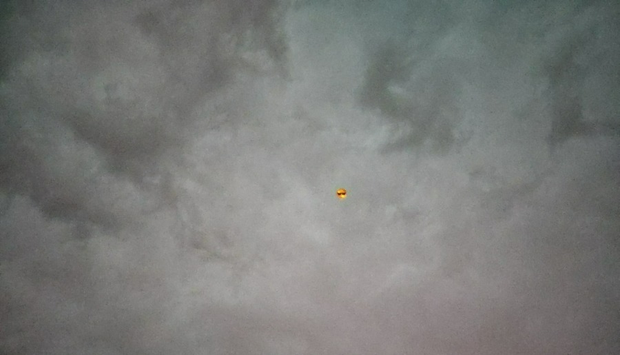 Auf dem Bild sieht man den von dunklen Gewitterwolken verhangenen Himmel und in der Mitte einen kleinen Luftballon, der ein Emoji mit Sonnenbrille darstellt.