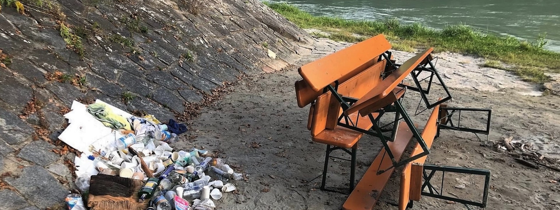 Foto: Ein Haufen (Party-)Müll (vor allem Flaschen) neben Bierbänken an einem Flussufer