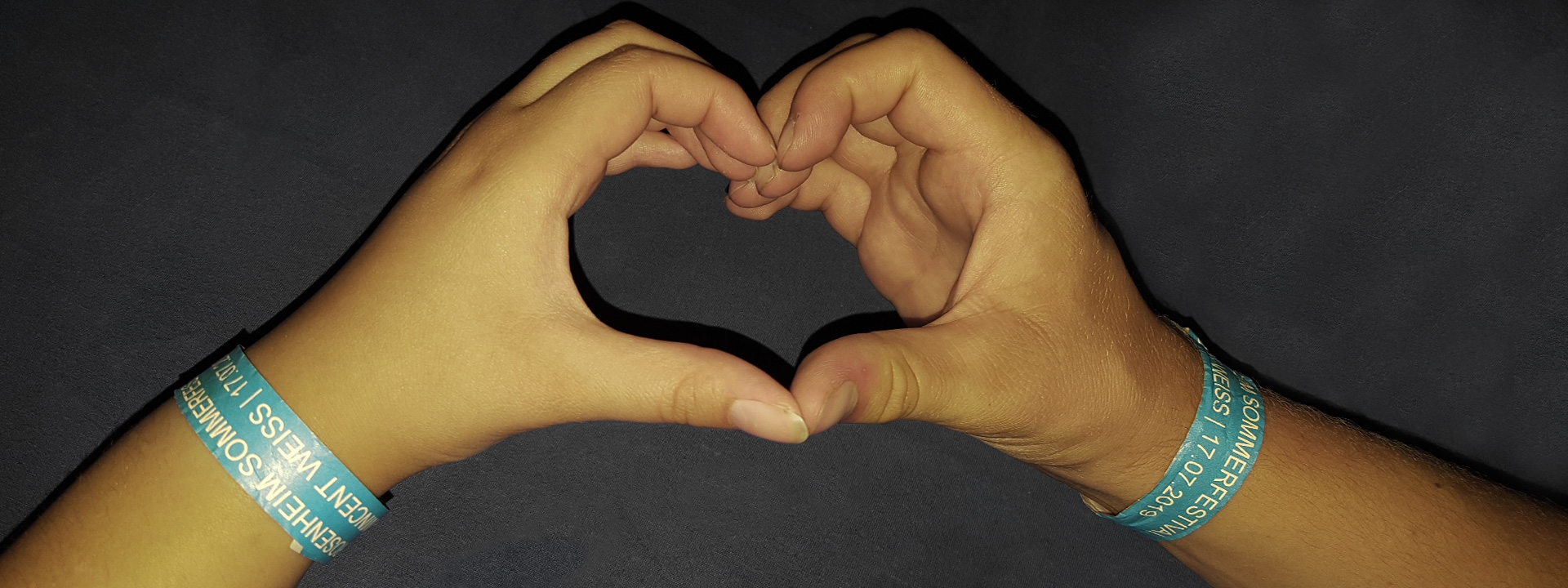Foto von zwei Händen, die ein Herz formen und die Festivalarmbänder tragen.
