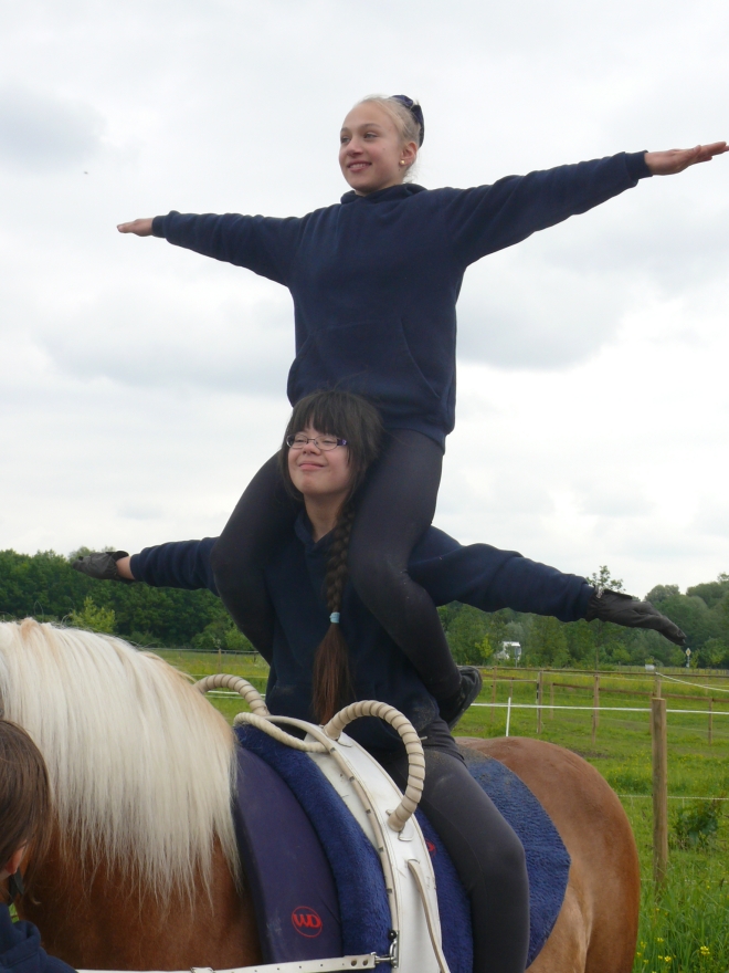 Foto: Auf einem Pferd sitzt eine Jugendliche und auf deren Schulter eine weitere