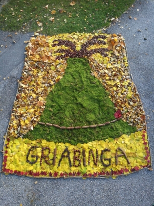 Foto: Ein großes Kunstwerk aus viel Herbstlaub, Moos und Tannenzapfen, das einen riesigen Trachenthut zeigt und den Schriftzug Griabinga