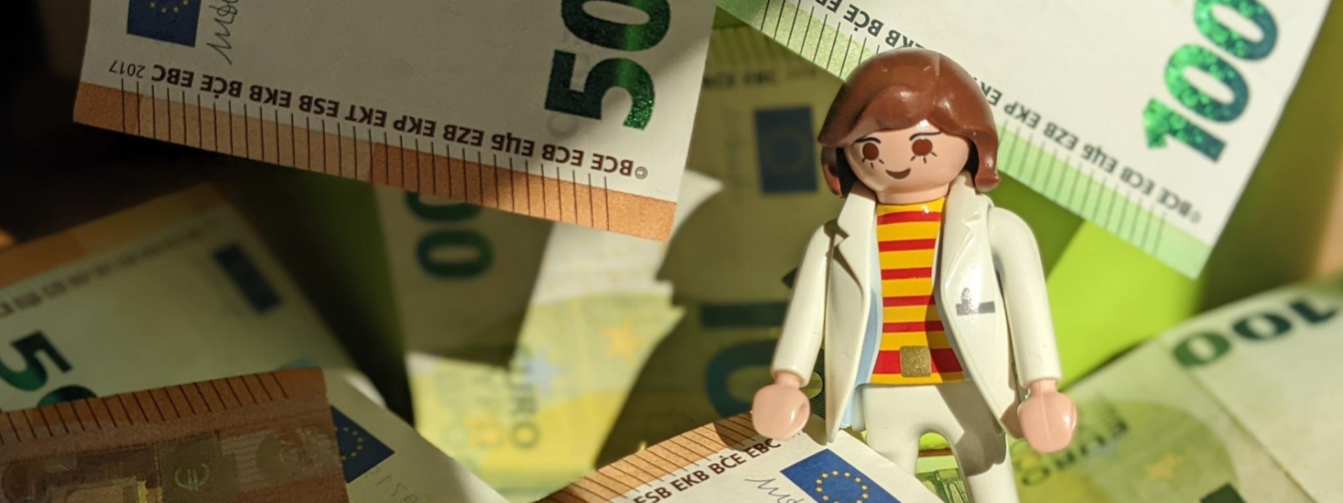 Foto: Eine weibliche Playmobil-Figur steht inmitten von Euro-Scheinen im Wert von 50 und 100 Euro
