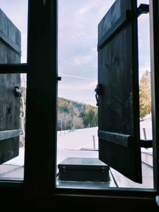Foto: Blick aus einem leicht geöffneten Fenster in eine verschneide Berglandschaft