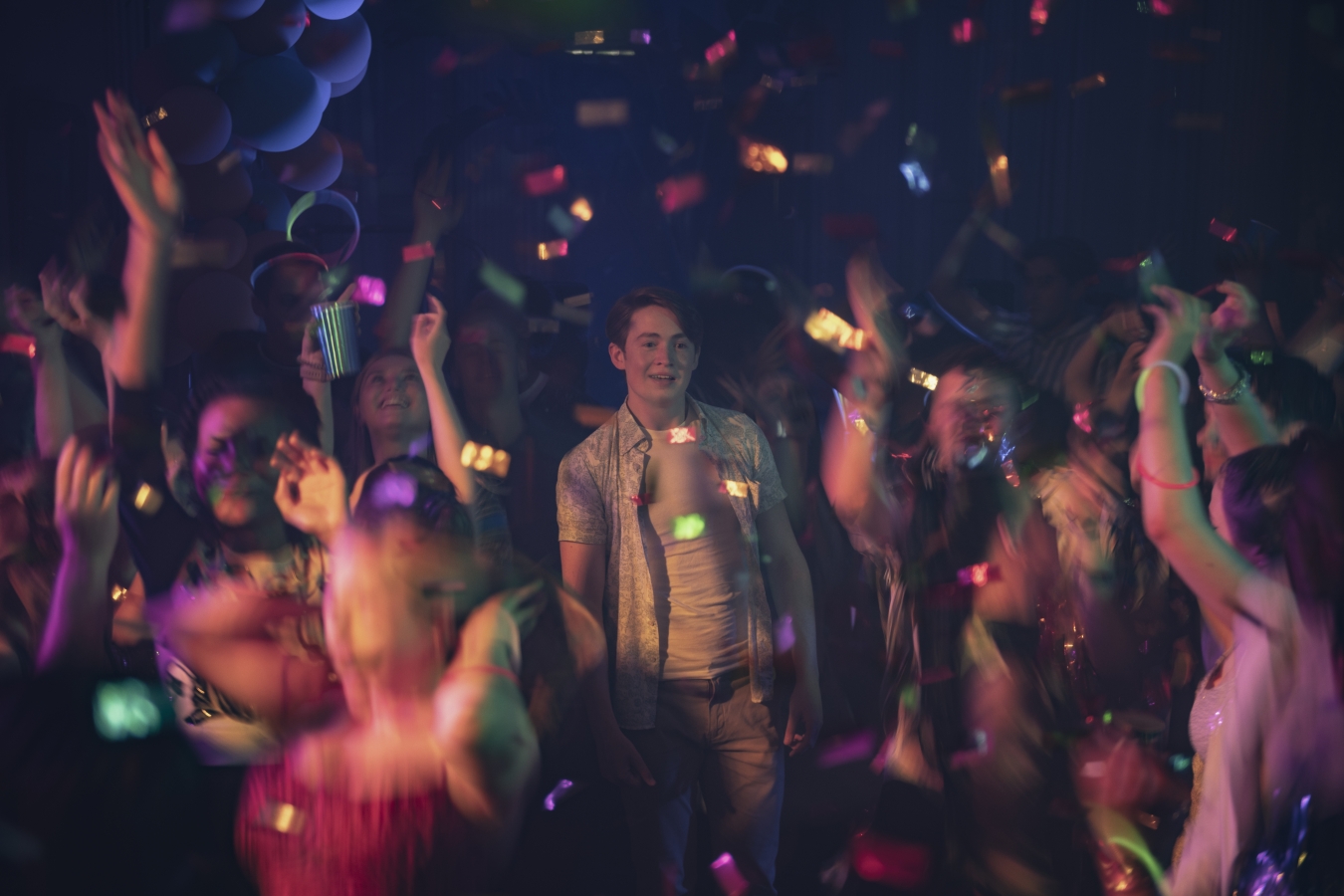 Nick steht auf einem Dancefloor und schaut lächelnd in die Runde, umringt von feiernden Menschen