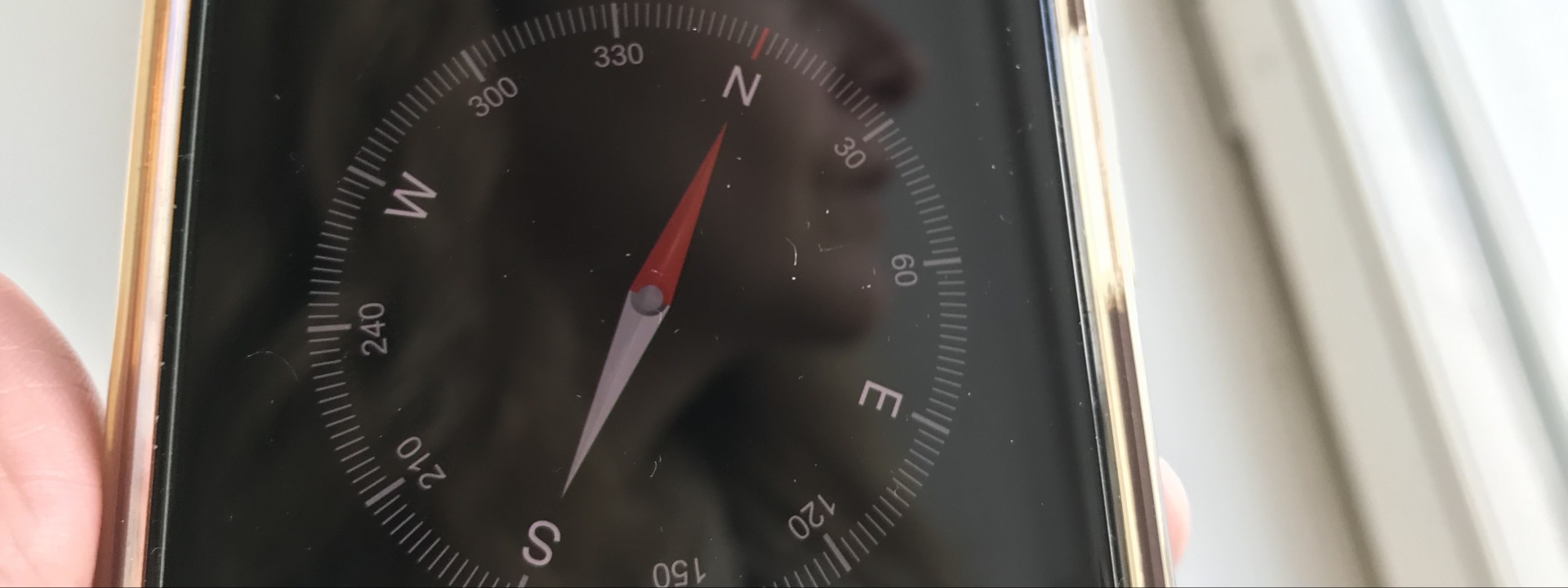 Wo soll es hingehen? | Foto: aROund Foto: Ein etwas verstabtes Smartphone in einer hand, darauf zu sehen ein Kompass und die Spiegelung eines weiblichen Gesichts im Profil