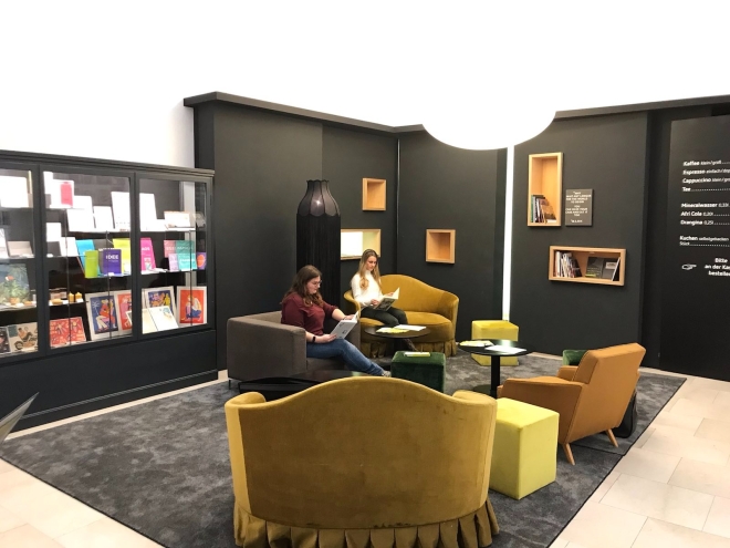 Foto: Ein Raum, eingerichtet wie eine Lounge mit Bücherregalen. Zwei junge Frauen sitzen dort in Sesseln und lesen.
