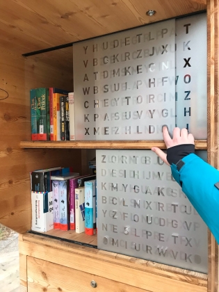 Foto: Ein Arm bewegt eine Schiebetüre zur Seite. Dahinter stehen mehrere Bücher.