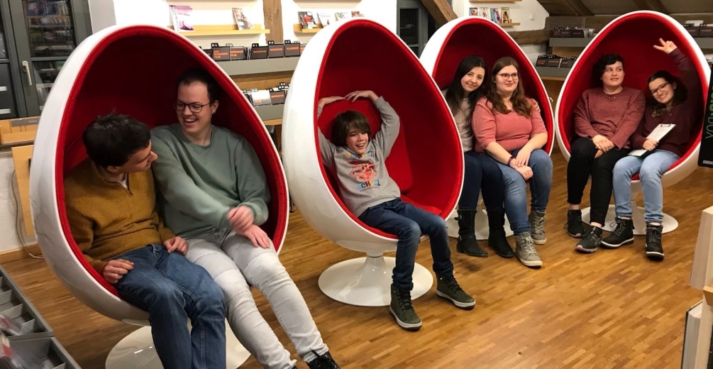 Foto: In 4 futuristischen Stühlen, die wie spacige Eier geformt sind, sitzen 7 junge Leute