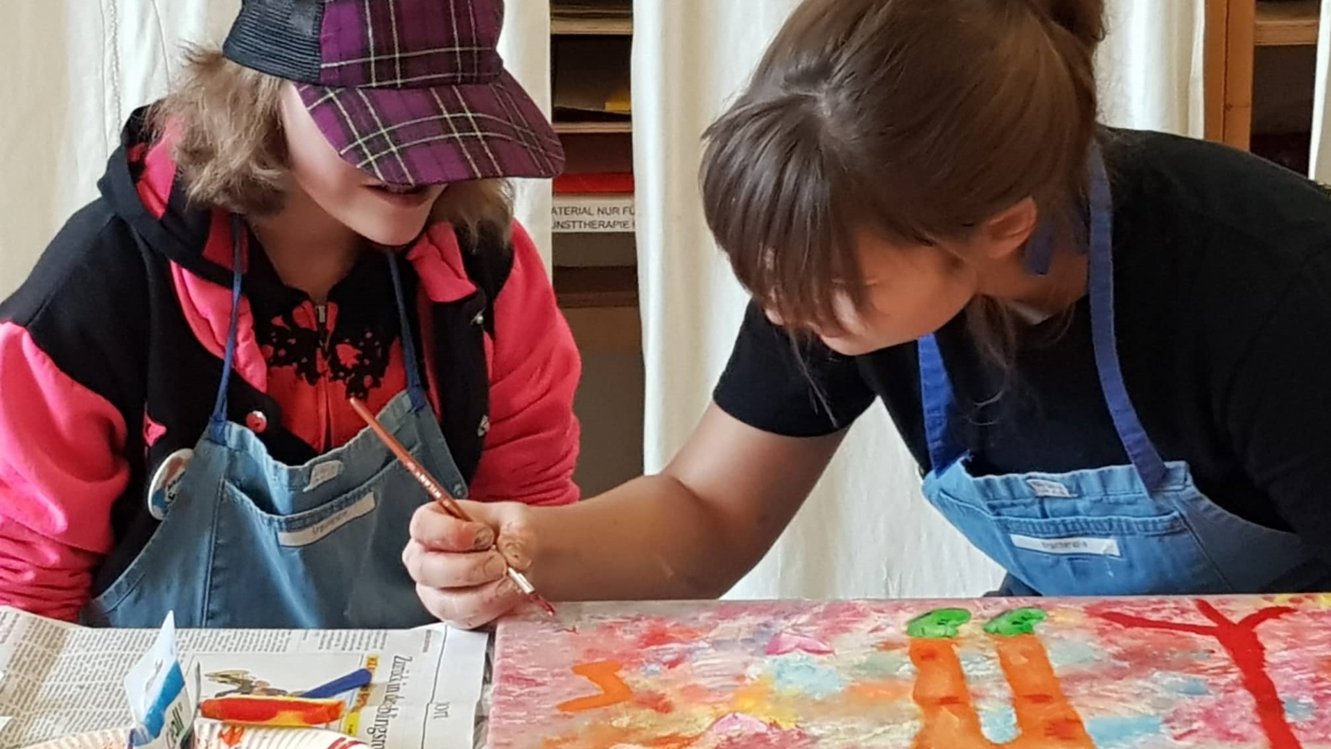 Foto von zwei Jugendlichen mit und ohne Einschränkung, die mit Pinsel und Farbe ein gemeinsames Bild malen.