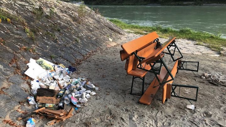 Foto: Ein Haufen (Party-)Müll (vor allem Flaschen) neben Bierbänken an einem Flussufer