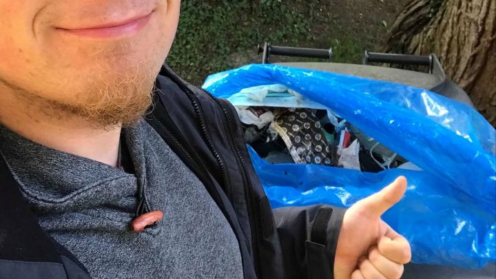 Foto: Daumen hoch vor gesammeltem Müll in einem blauen Sack