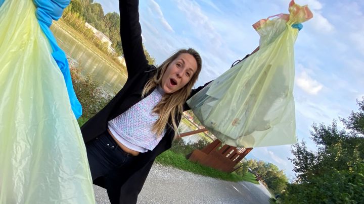 Foto: Eine Frau macht Quatsch und lacht. Sie hält ihre Mülltüte in die Höhe.