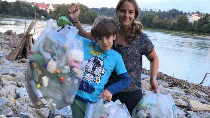 Foto: Eine Frau und ein Junge zeigen ihre drei vollen Müllsäcke an einem Flussufer