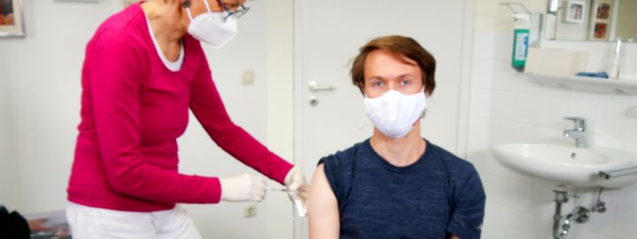 Foto: Ärztin impft Patienten. Beide tragen Masken.