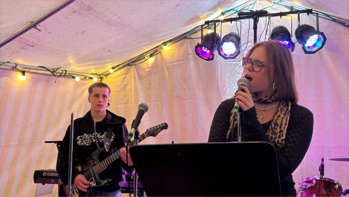 Foto: bei einem kleinen Konzert in einem bunt beleuchteten Zelt singt ein Mädchen. Im Hintergrund spielt ein Junge Bass.