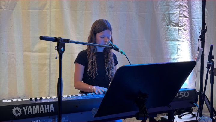 Foto: bei einem kleinen Konzert in einem beleuchteten Zelt spielt ein Mädchen Keyboard.