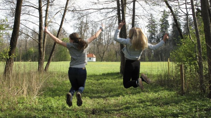 Foto: zwei Freundinnen im Wald von hinten, sie machen einen Luftsprung