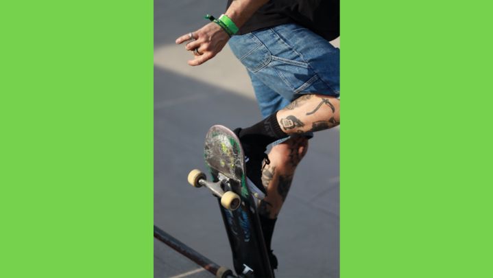 Foto: eine Nahaufnahme von einem Skater, der gerade einen Trick an der Kante einer Quarterpipe macht. Der Ausschnitt zeigt nur das Skateboard und die tatoowierten Beine des Skaters.