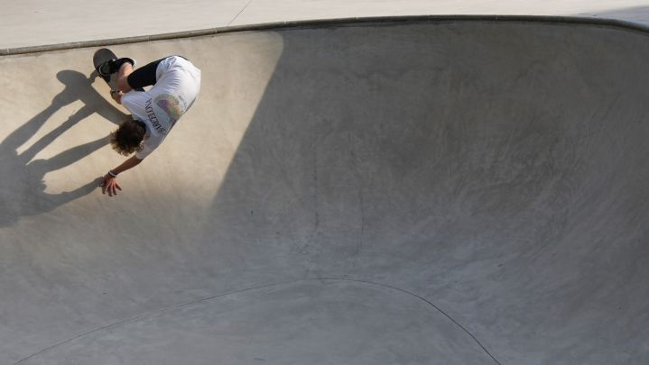 Foto: ein Skateboarder in einem "Pool" aus Beton. Er macht einen Trick an der Kante des Pools und sein Schatten fällt auf den Beton.