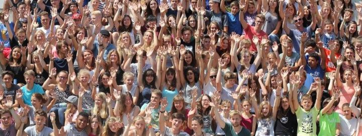 Ein Gruppenfoto mit ca. 100 jungen Menschen, die jubelnd die Hände in die Höhe halten