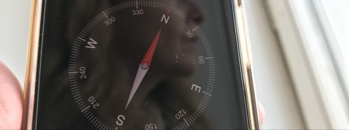 Wo soll es hingehen? | Foto: aROund Foto: Ein etwas verstabtes Smartphone in einer hand, darauf zu sehen ein Kompass und die Spiegelung eines weiblichen Gesichts im Profil