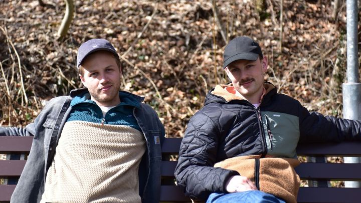 Foto: Gotti und Eisna sitzen auf einer Parkbank und lächeln nett in die Kamera.