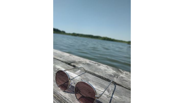 Foto: Sonnenbrille auf einem hölzernen Steg. Im Hintergrund ist der See.