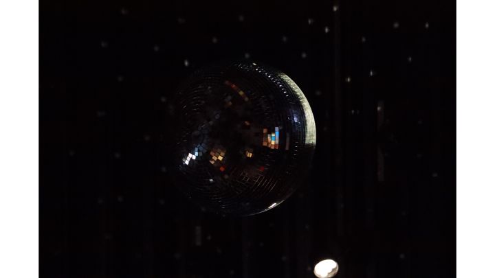 Foto: Eine Discokugel von unten. Der Raum ist dunkel, nur von rechts ist sie beleuchtet.