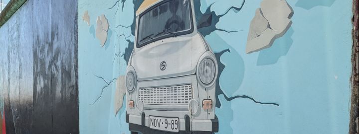 Foto von einem Teil der Berliner Mauer an der East Side Gallery: Auf einem Gemälde durchbricht ein Trabbi die Mauer