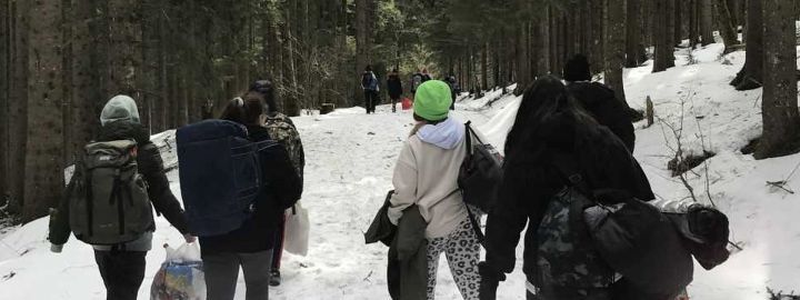 Foto: Junge Leute mit Rücksäcken und Umhängetaschen auf einem verschneiten Waldweg