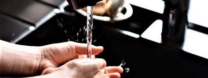 Auf dem Bild erkennt man eine schwarze Spüle und zwei Hände, die unter laufendem Wasser gewaschen werden.
