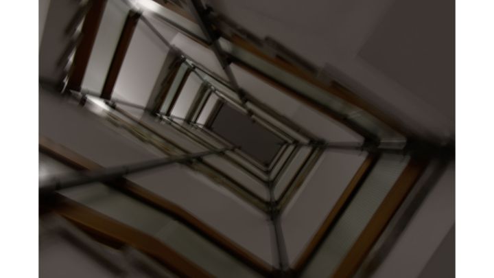 Foto: Ein Treppenhaus von unten nach oben fotografiert. Unscharf erkennt man den Handlauf mehrerer Stockwerke.